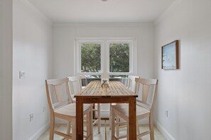 A dining area with a wooden table and four chairs, a window with a view of trees, and a framed picture on the wall. - Close to Beach Couple's Retreat (Hilton Head Island)