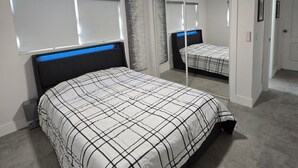 A bedroom with a bed, a ceiling fan, a window, and a mirror. - Cozy 2BD/1BA Near Beach + Fast I-95 Access! (Hallandale Beach)