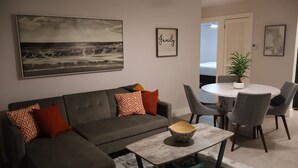 A living room with a grey sofa, a coffee table, and a dining area with grey chairs and a white table. - Cozy 2BD/1BA Near Beach + Fast I-95 Access! (Hallandale Beach)