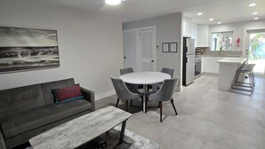 A modern living room with a gray sofa, a round dining table, and a ceiling fan. - Cozy 2BD/1BA Near Beach + Fast I-95 Access! (Hallandale Beach)