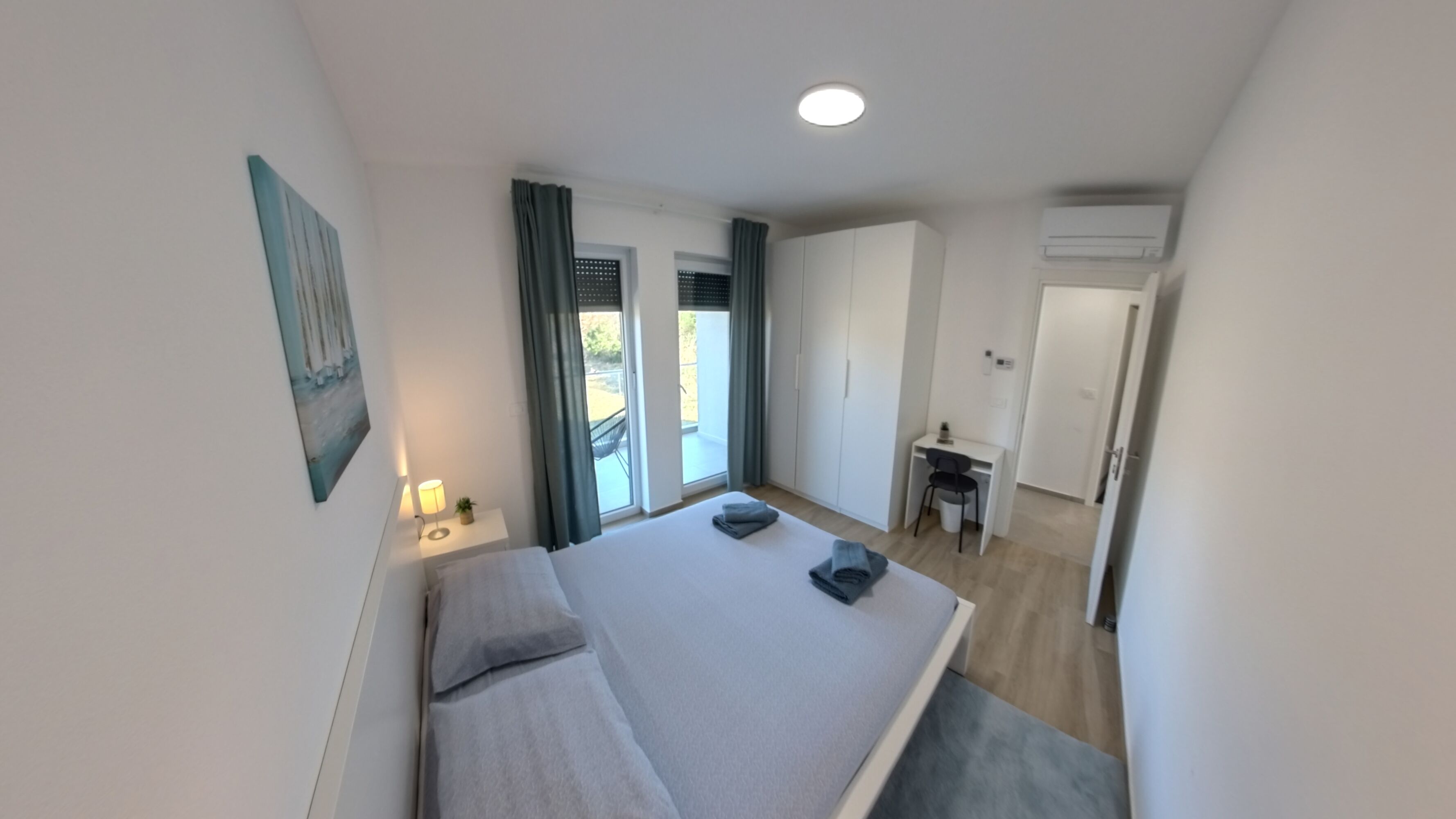 A modern bedroom with a bed, bedside table, lamp, and a view of the outdoors.