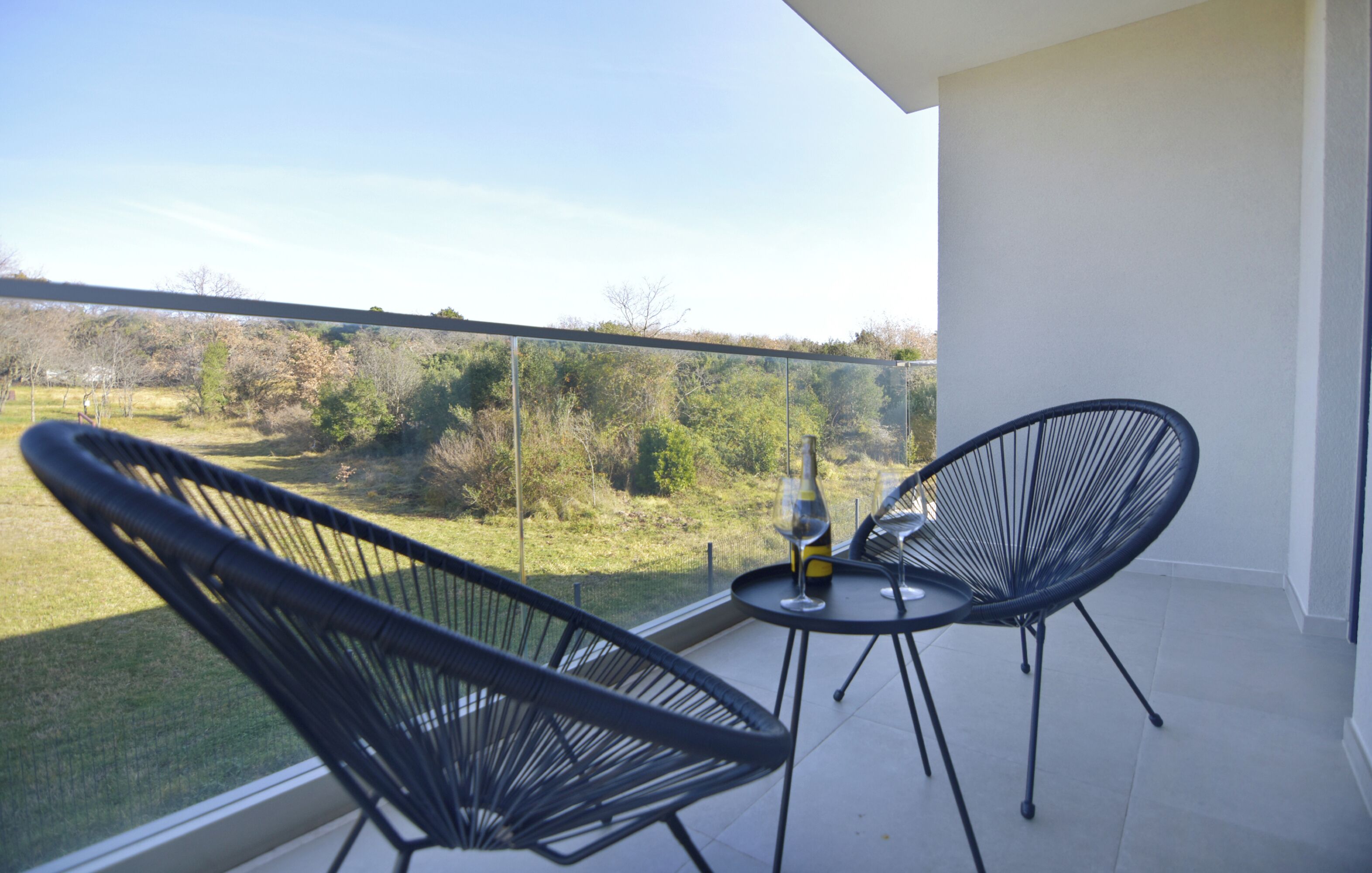 A balcony with two black chairs and a small table with a wine glass.