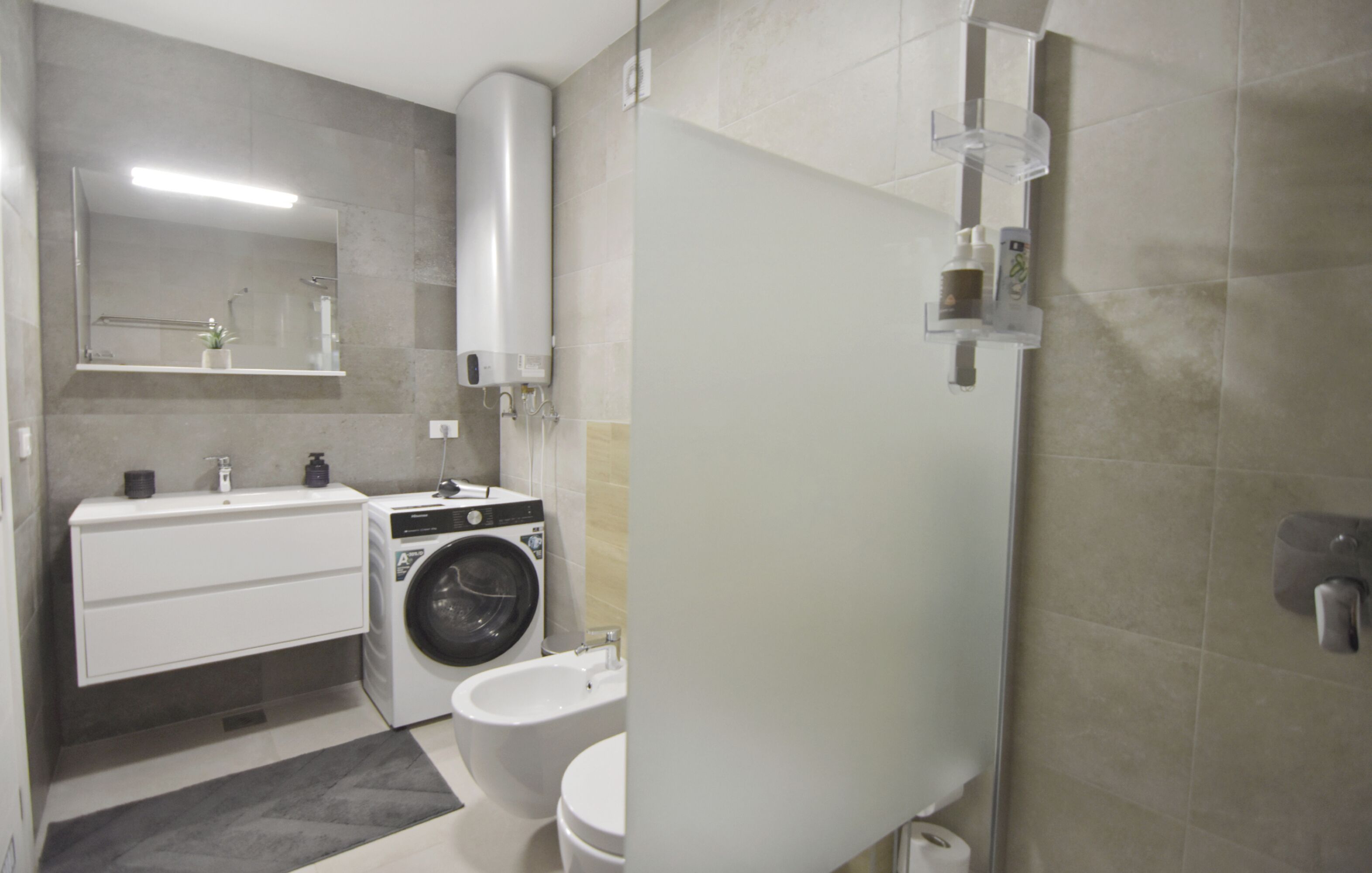 A modern bathroom with a washing machine, toilet, and a large mirror.