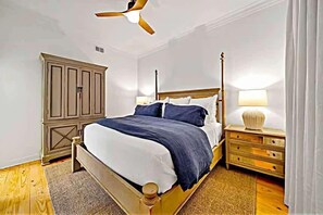 Une chambre à coucher comprenant un lit, des tables de chevet, une armoire et un ventilateur de plafond.