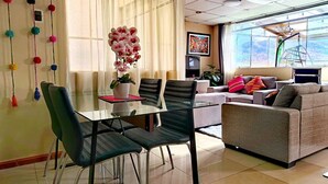 A modern living room with a glass dining table, black chairs, a grey sofa, and a large window with a view. - Cozy Apartment with View of Historic Cusco - Excellent Location-600Mbps (Cusco)