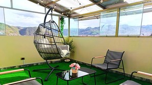 A room with a hanging chair, two cushioned chairs, a small table with a vase, and a view of mountains through large windows. - Cozy Apartment with View of Historic Cusco - Excellent Location-600Mbps (Cusco)