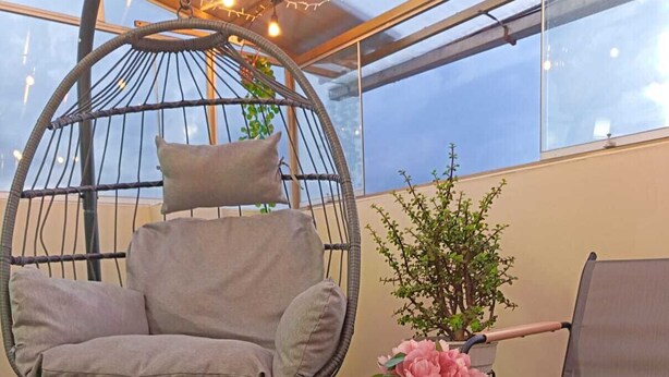 A cozy outdoor seating area with a hanging chair, a cushioned bench, a table with a book and a cup, and a potted plant. - Cozy Apartment with View of Historic Cusco - Excellent Location-600Mbps (Cusco)