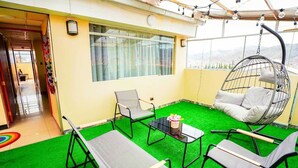 A room with a green artificial turf floor, a hanging chair, a table with a vase, and a window with curtains. - Cozy Apartment with View of Historic Cusco - Excellent Location-600Mbps (Cusco)