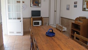 Ruokailutila, jossa on puinen pöytä, tuoleja, sininen kulho, mikroaaltouuni ja televisio puisen jalustan päällä.