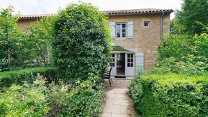 A stone building with a tiled roof, a paved pathway, and lush greenery. - Gîte “La Gariotte” with Shared Pool and Jacuzzi (Montcabrier)