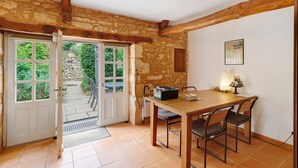 A room with a wooden table, chairs, a door leading outside, and a stone wall. - Gîte “La Gariotte” with Shared Pool and Jacuzzi (Montcabrier)