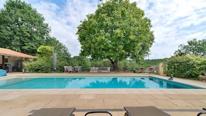 A swimming pool with lounge chairs, a covered seating area, and a large tree in the background. - Gîte “La Gariotte” with Shared Pool and Jacuzzi (Montcabrier)
