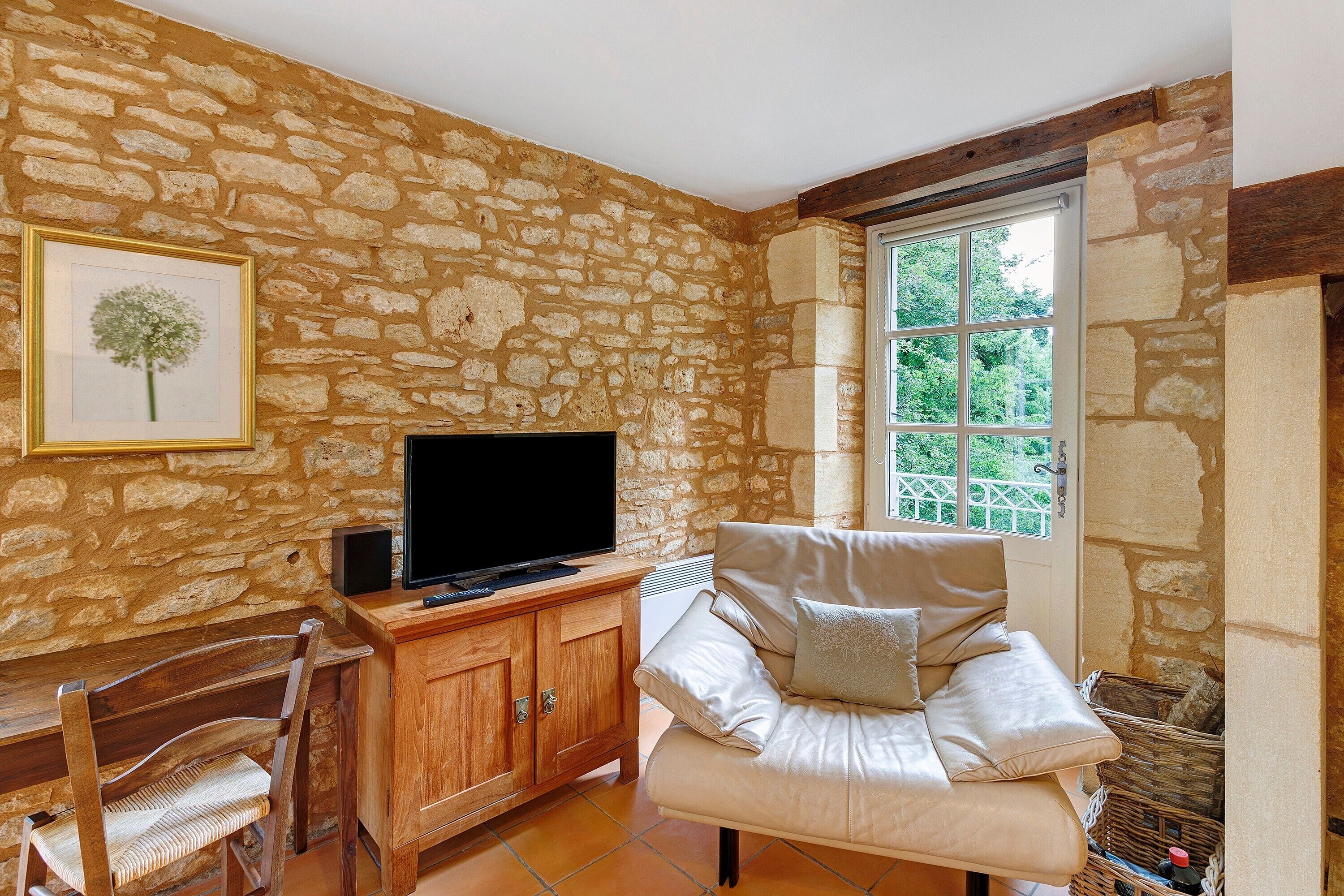 A stone-walled room with a television, a sofa, a chair, and a framed picture on the wall.