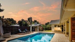 Une piscine rectangulaire avec une terrasse carrelée, entourée d’une clôture en bois et d’un patio couvert.