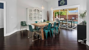 Un vaste espace de salle à manger avec une table en bois et des chaises de couleur turquoise, un buffet blanc et une vue sur une terrasse extérieure avec une piscine.