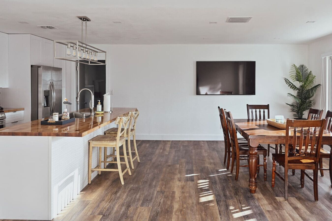 Una cucina moderna con isola in legno, zona pranzo con tavolo e sedie, e televisore a schermo piatto montato a parete.