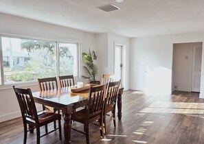 A dining area with a wooden table and chairs, large windows, and a potted plant. - Dockside Getaway - Gulf Access & Putting Green (Cape Coral)