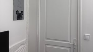 A white door with a simple design, a small picture frame with a Mickey Mouse silhouette and the text "YOU ARE MAGIC" on the wall, and a red bench in the foreground. - Appartement 2 Chambres Business Famille (Orléans)