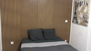 Ein modernes Schlafzimmer mit einem Kopfteil aus Holzleisten, einem Bett mit grauem Bettzeug und Wandbild mit Paris-Motiv.
