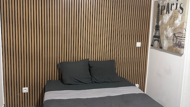 A modern bedroom with a wooden slat headboard, a bed with grey bedding, and a Paris-themed wall art. - Appartement 2 Chambres Business Famille (Orléans)