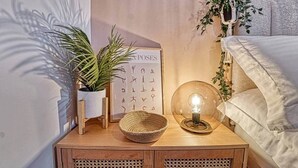 Una mesita de noche ordenada con una planta en maceta, un cartel enmarcado, una cesta tejida y una lámpara de vidrio transparente.