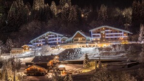 Un rifugio coperto di neve con luci esterne illuminate, circondato da alberi e un paesaggio innevato.