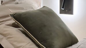 Un letto con biancheria beige e un cuscino verde.