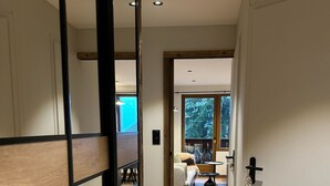 Un corridoio con pavimento in legno, una porta scorrevole e vista su un soggiorno con divano e tavolino.