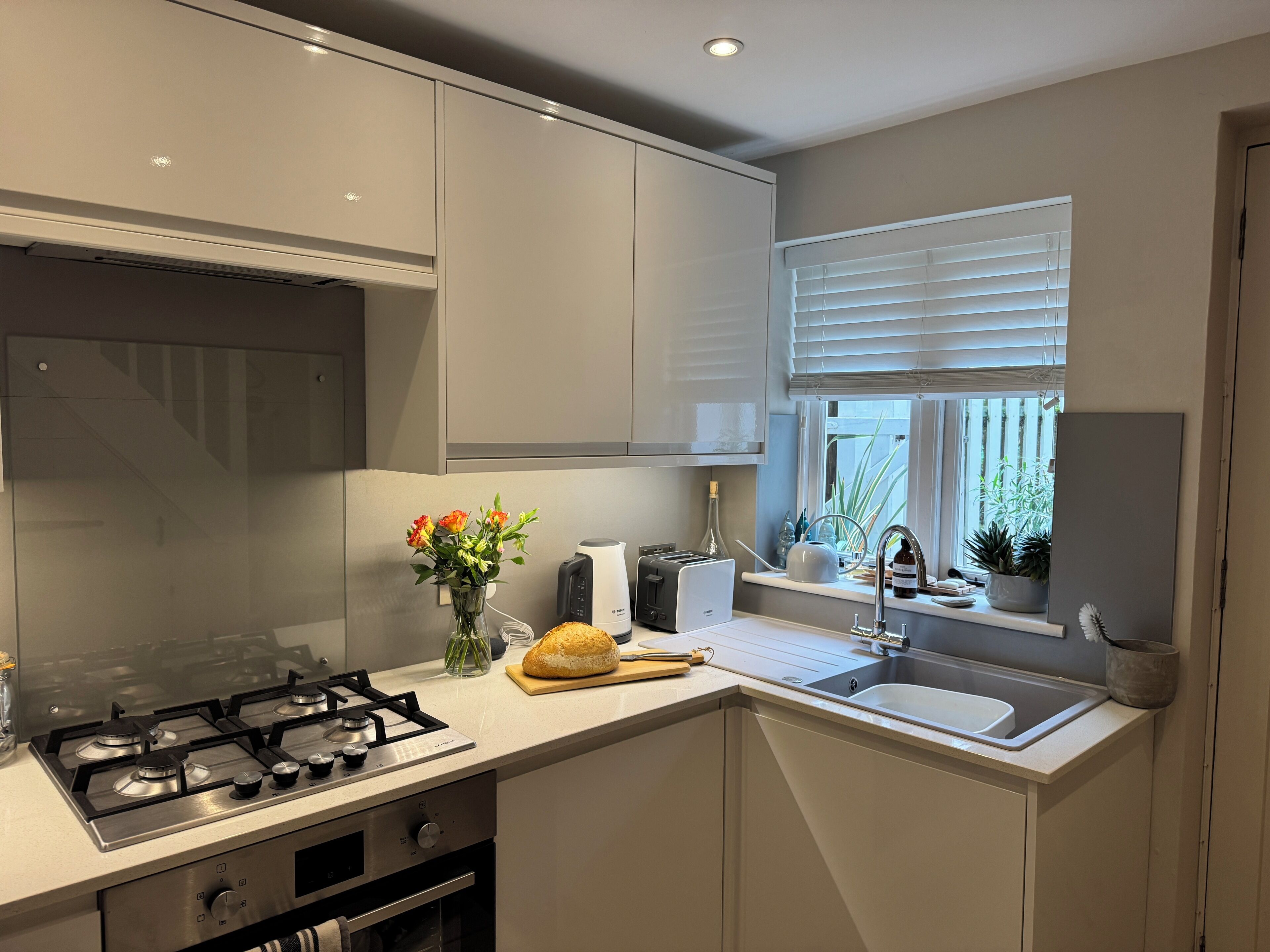 A modern kitchen with a gas stove, a built-in oven, a sink, and a window with blinds.
