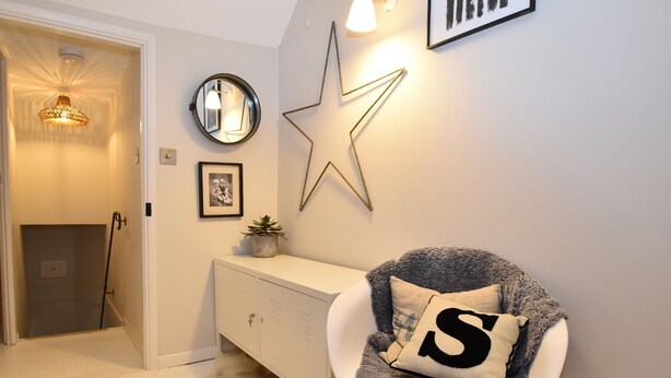 Een kamer met een witte kast, een decoratie in de vorm van een ster, een ronde spiegel en een stoel met een kussen in de vorm van een 'S'.