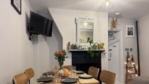 Een eetruimte met een ronde tafel, houten stoelen, een vaas met bloemen en een open haard.