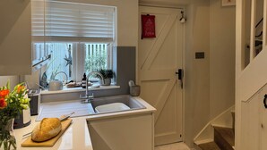 Een moderne keuken met een ingebouwd spoelbakje, een raam met zonwering, een aanrecht met een brood en een rood bordje op de deur.