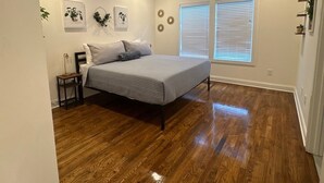 A bedroom with a bed, a ceiling fan, two windows with blinds, and a wooden floor.
