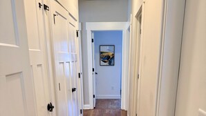 A hallway with wooden flooring, white doors, and a ceiling light fixture.