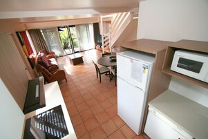 Cocina compacta con refrigerador, microondas y un pequeño comedor con mesa y sillas.