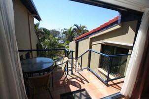Un balcón con mesa y sillas, vista de los alrededores y un tejado rojo.