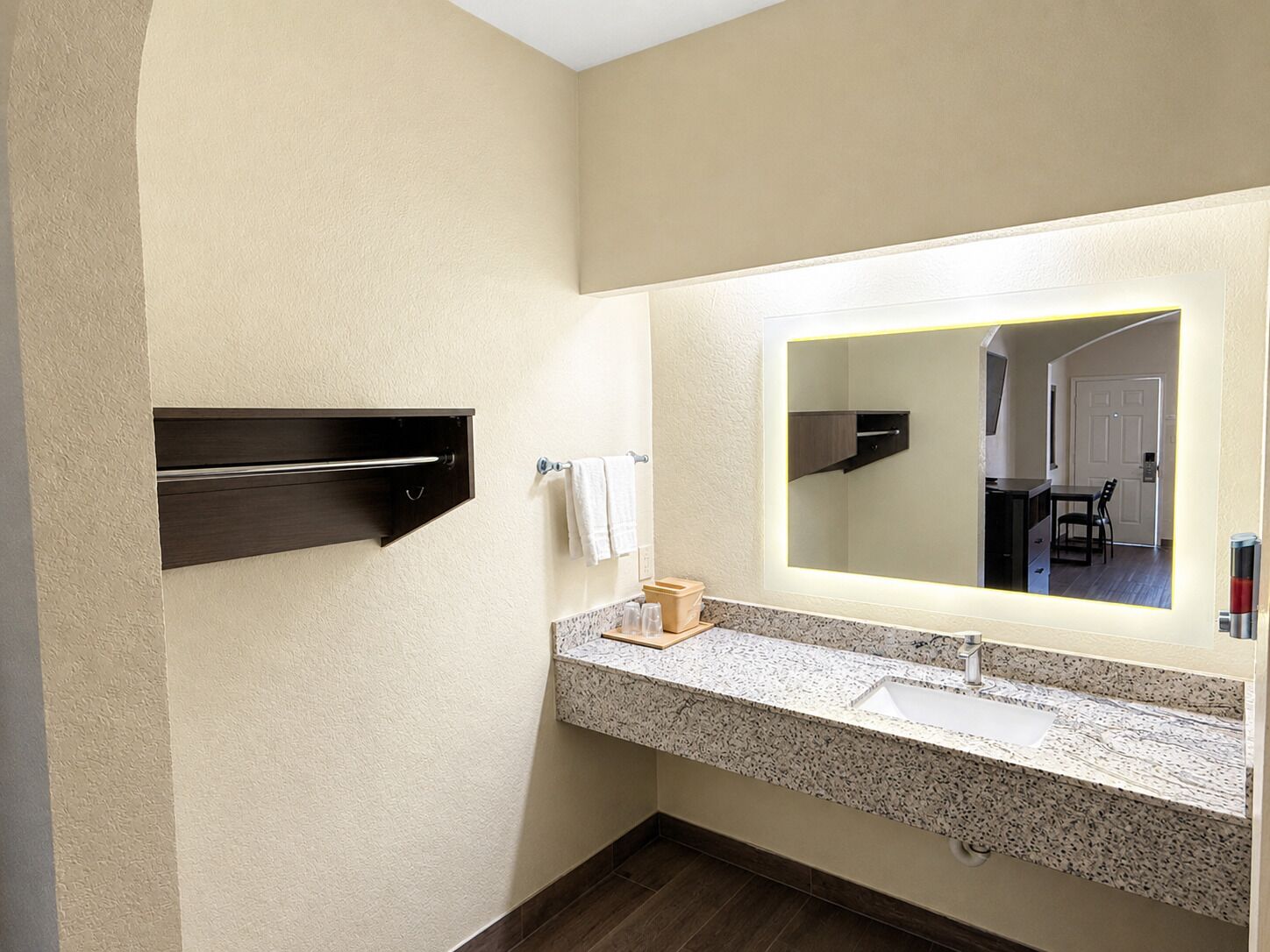 Un baño con encimera de granito, lavamanos, espejo y toallero.