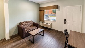 Um quarto com sofá, uma mesinha, janela com cortinas, porta e radiador.