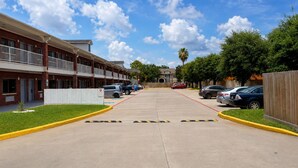 Um hotel com vários andares, um estacionamento, uma galeria coberta e uma fileira de carros estacionados na rua.