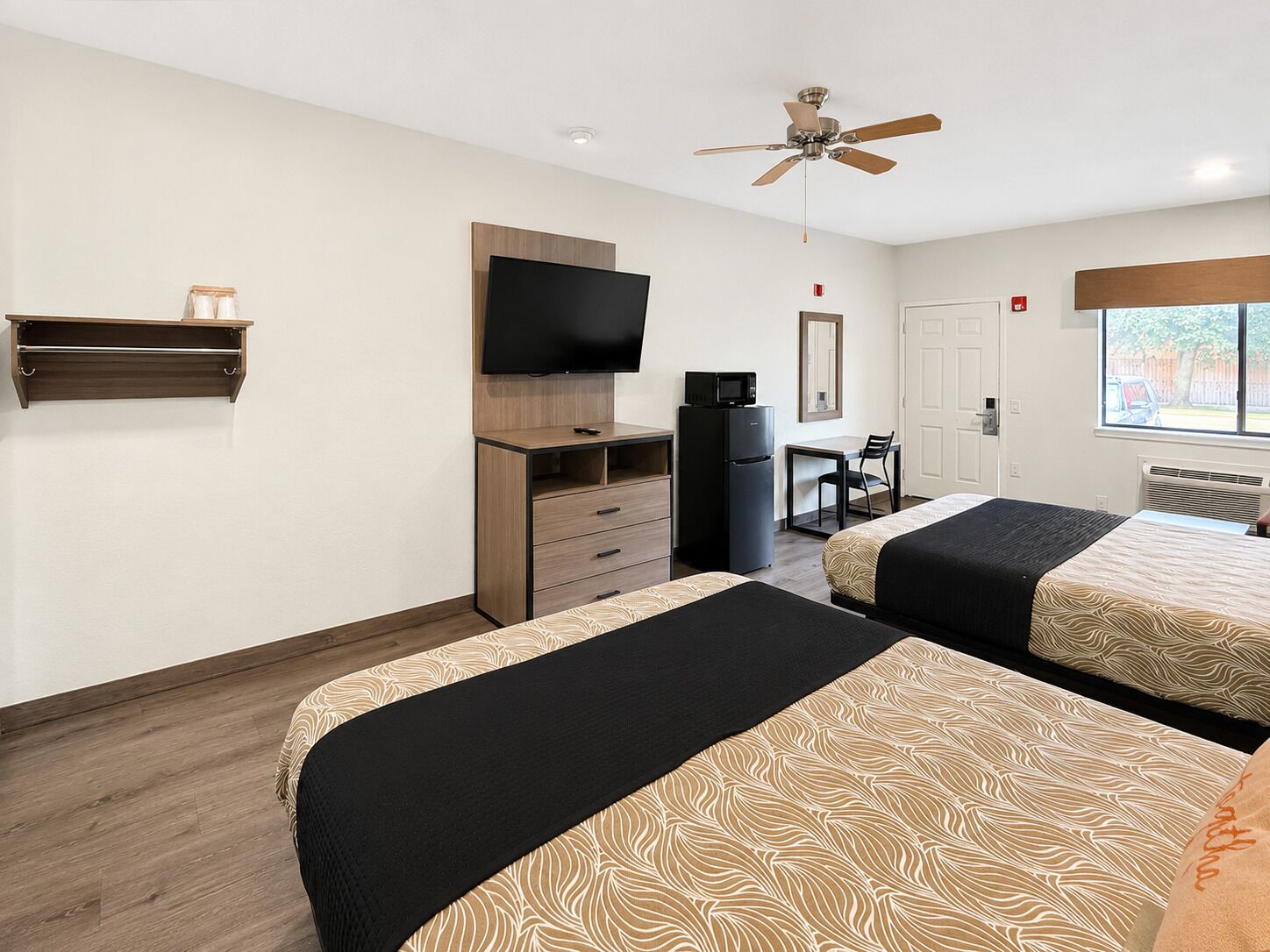A hotel room with two beds, a TV, a desk, a chair, a microwave, and a ceiling fan.