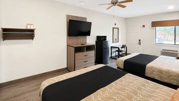 A hotel room with two beds, a TV, a desk, a chair, a microwave, and a ceiling fan.