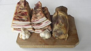 A wooden cutting board with several pieces of bacon and two garlic bulbs.