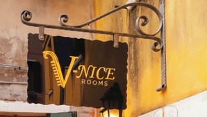 Une enseigne d’hôtel portant le nom « V-NICE ROOMS » et un luminaire décoratif placé au-dessus.