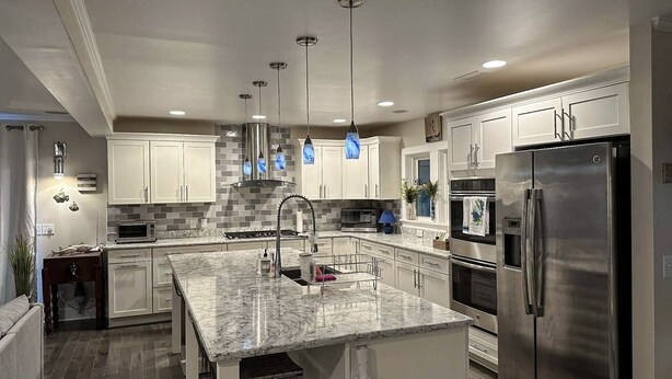 A modern kitchen with white cabinets, a stainless steel refrigerator, and a marble countertop. - IR56: Beach Belle: Serene Marsh Views (Ocracoke)
