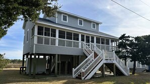 A two-story house with a covered porch and a staircase leading to the upper level. - IR56: Beach Belle: Serene Marsh Views (Ocracoke)