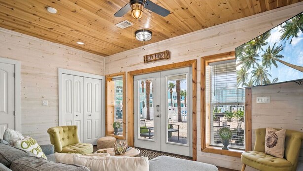 A cozy room with a wooden ceiling, a large window with a view of palm trees, and a sign that reads "Beach House".