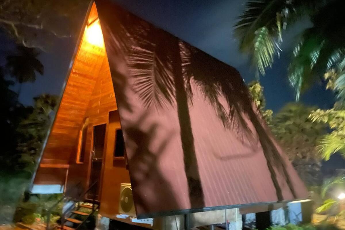 Een gebouw in een driehoekige vorm met een warme lichtbron bovenop, omringd door palmbomen.