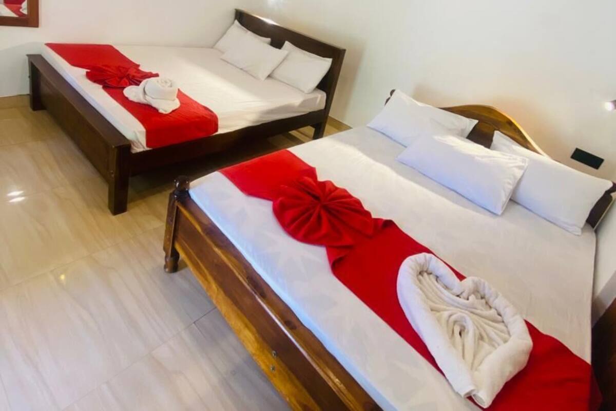 Twee enkele bedden met rode en witte beddengoed, een houten hoofdbord en een witte muur met een airconditioning.