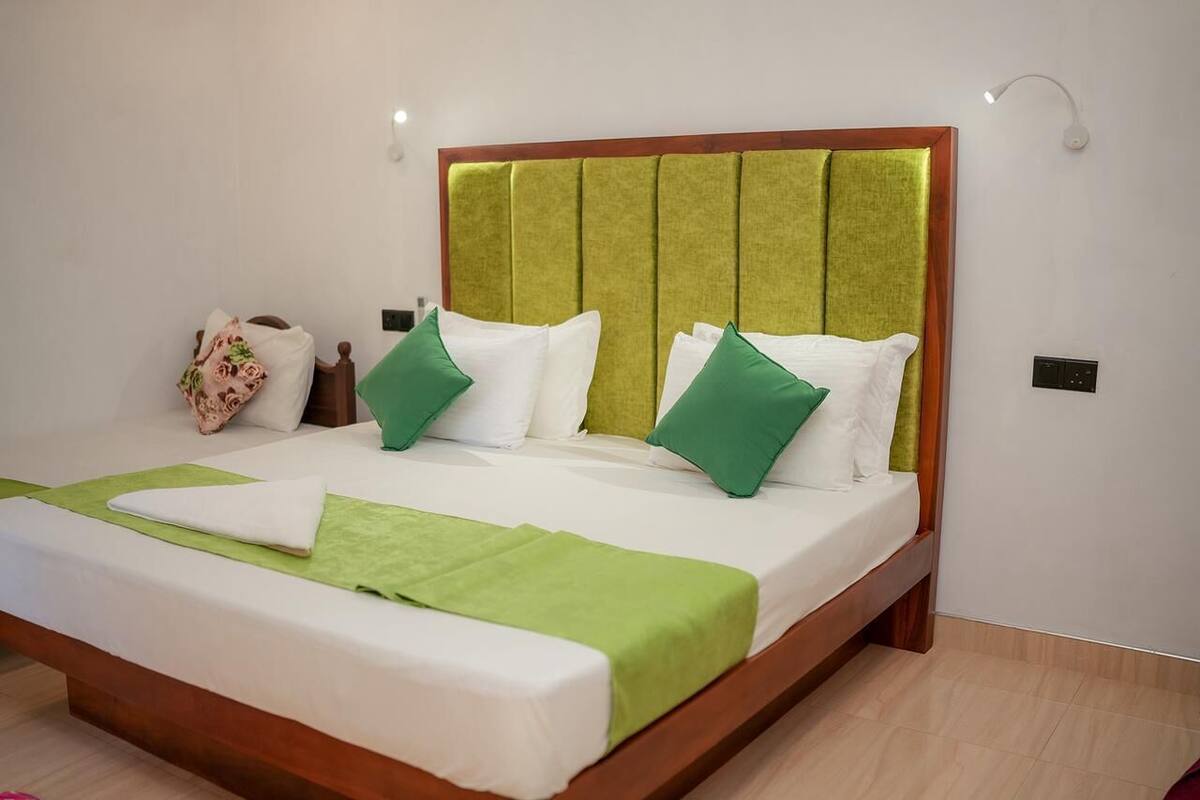 Een bed met een houten frame en een bekleden hoofdbord, wit beddengoed en groene kussens.
