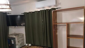 A compact room with a bed, a small table with a chair, a TV mounted on the wall, and a wardrobe with shelves. - Makgadikgadi Riverview Inn (Nata)
